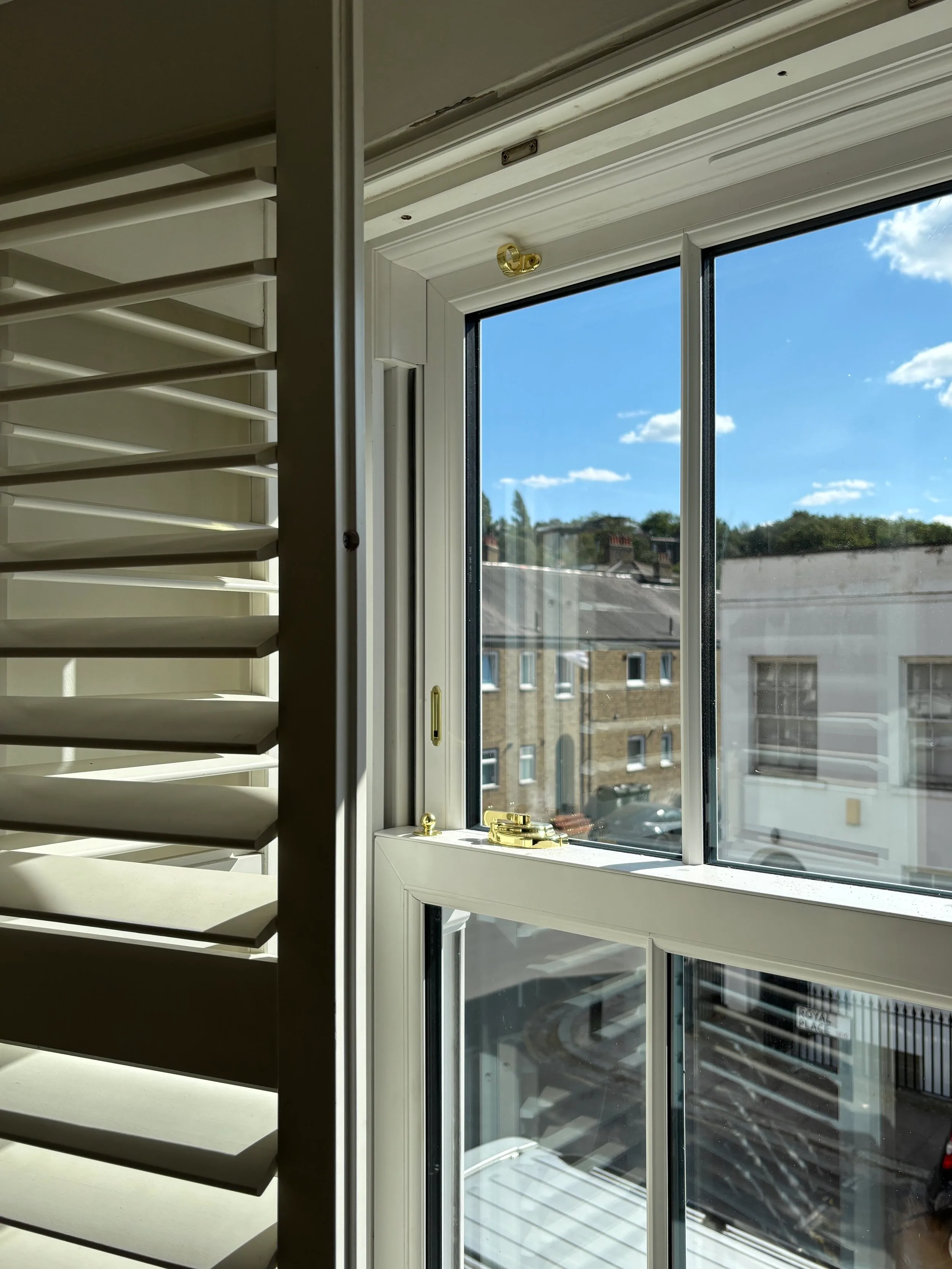 White sliding sash window seen from inside, with a wooden shutter folded back beside it