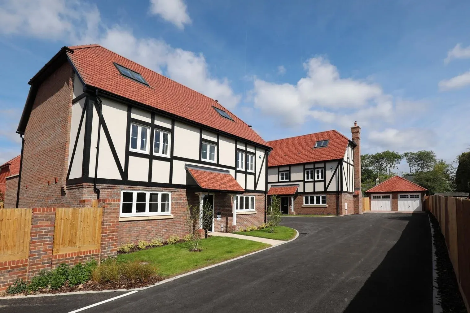 Newly finished mock Tudor houses with red tiled roofs and white casement windows beside a freshly laid private drive