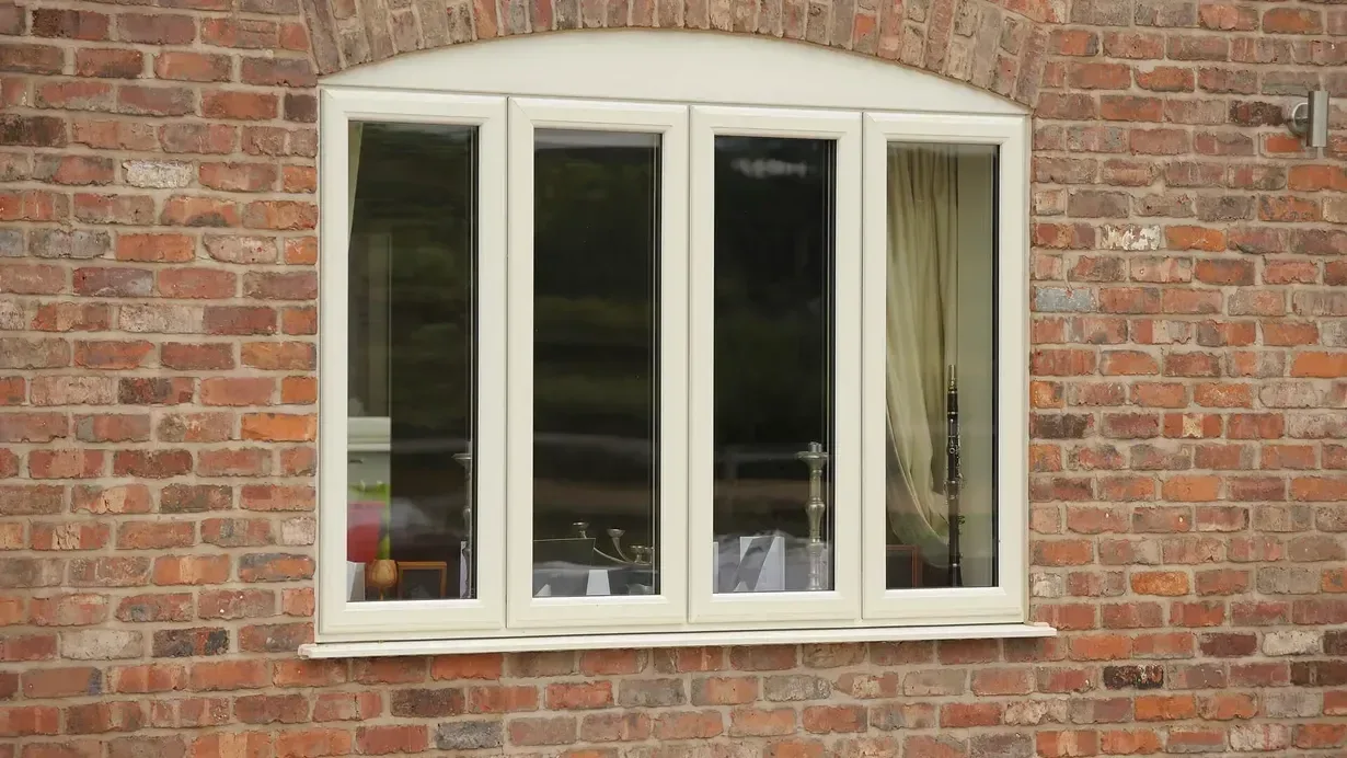 Cream uPVC casement window with four glazed panels in a red brick wall under a brick arch