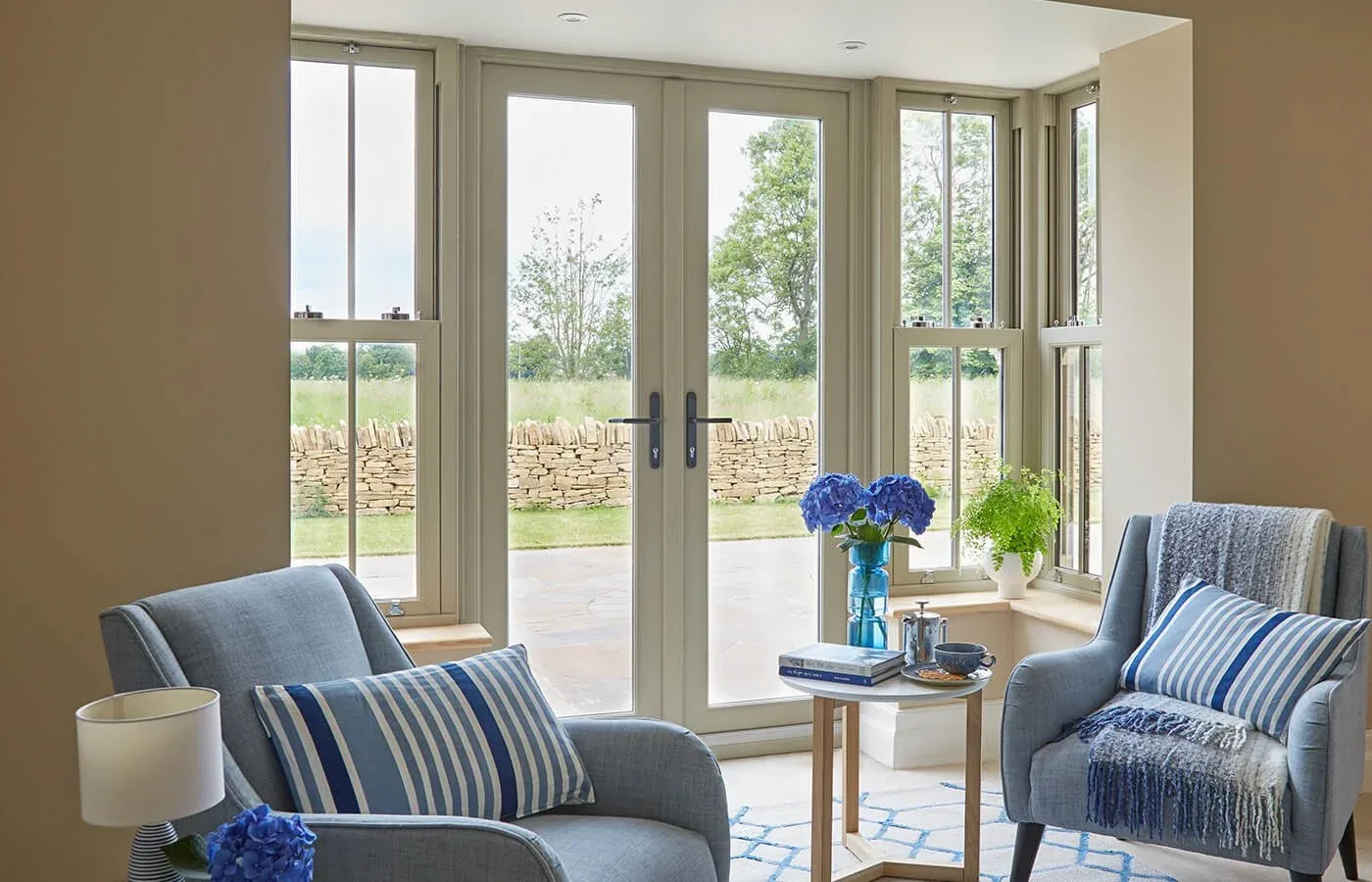 Living room with blue armchairs and cream French doors with matching side windows opening onto a patio