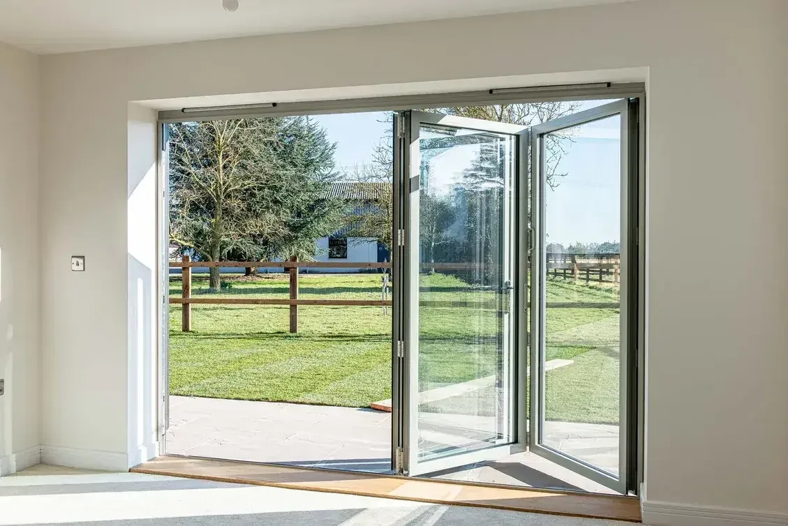 Agate grey aluminium bi-fold doors folded open from a bright room onto a lawn