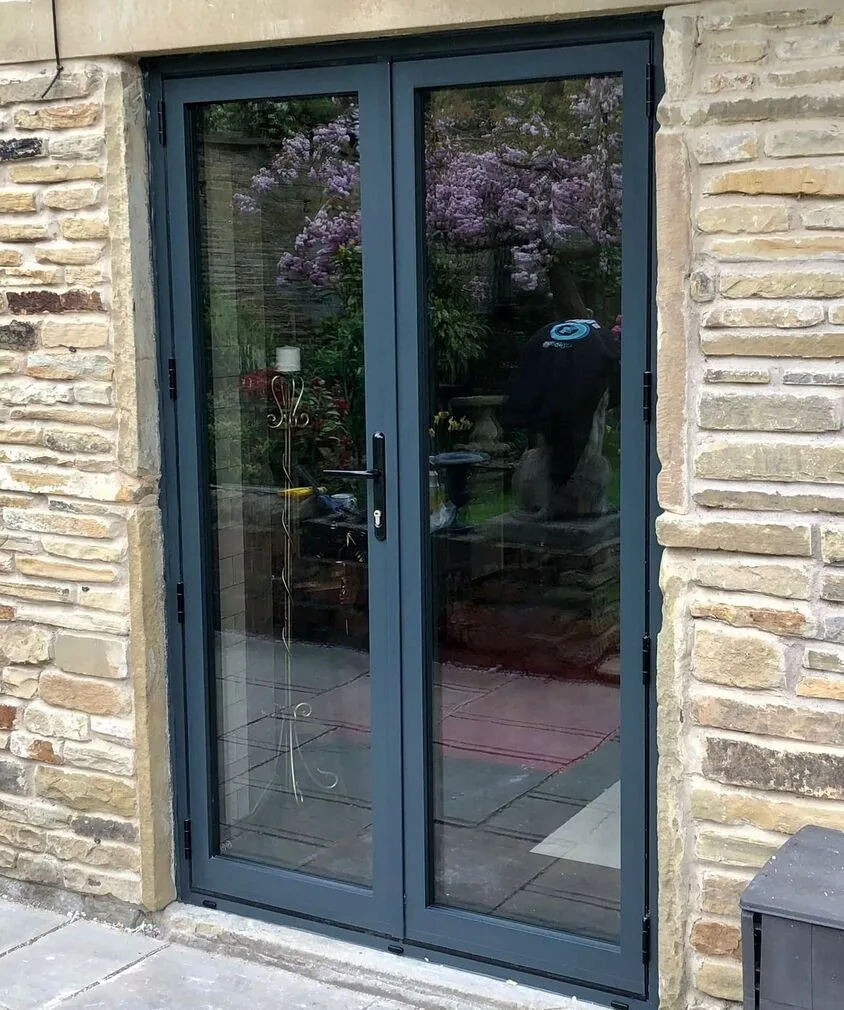 Dark grey aluminium French doors set in a stone wall, reflecting a garden in blossom