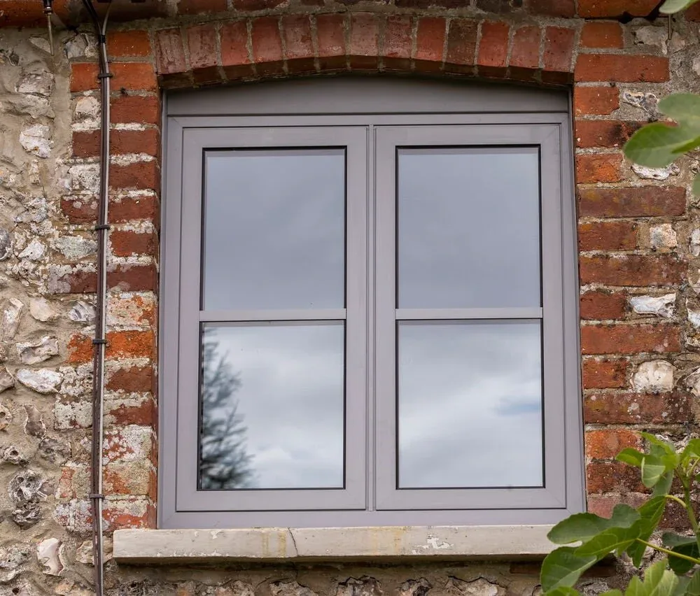 Grey flush sash window with glazing bars, set in a flint and red brick wall