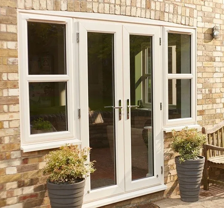 White uPVC French doors with matching side windows in a brick wall, with potted plants either side
