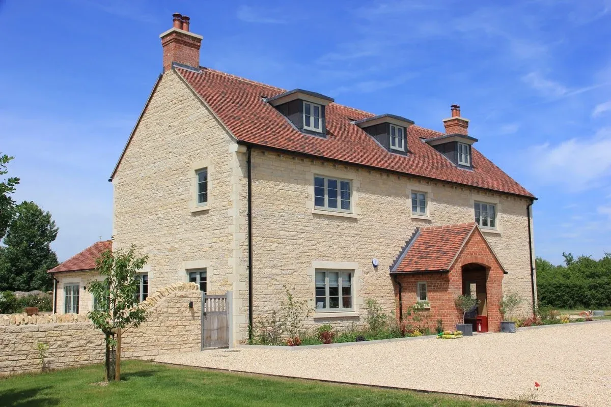 New-build stone house with a red tiled roof, dormer windows and a brick porch