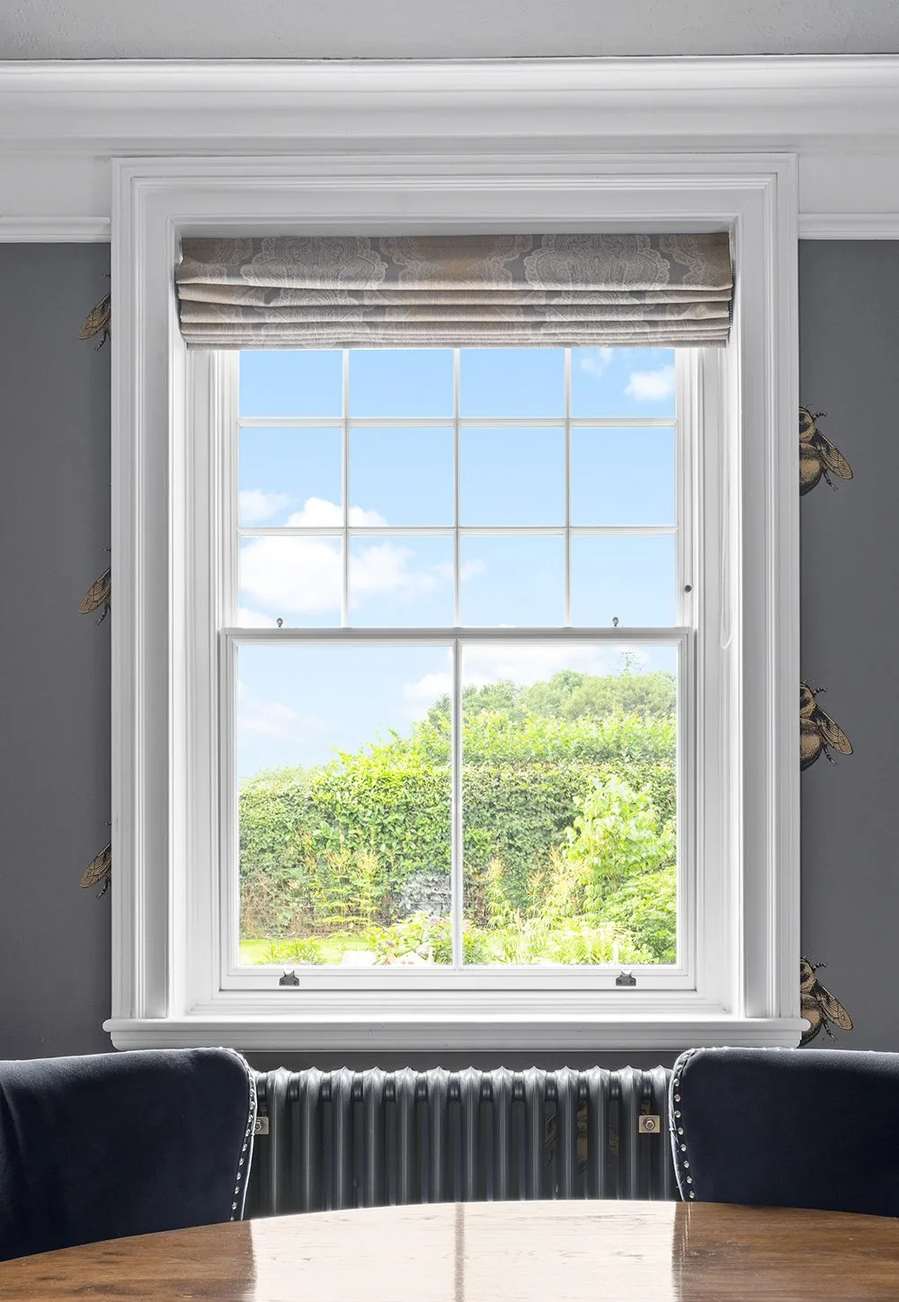White sliding sash window with Georgian bars and a Roman blind, seen from inside with a garden view