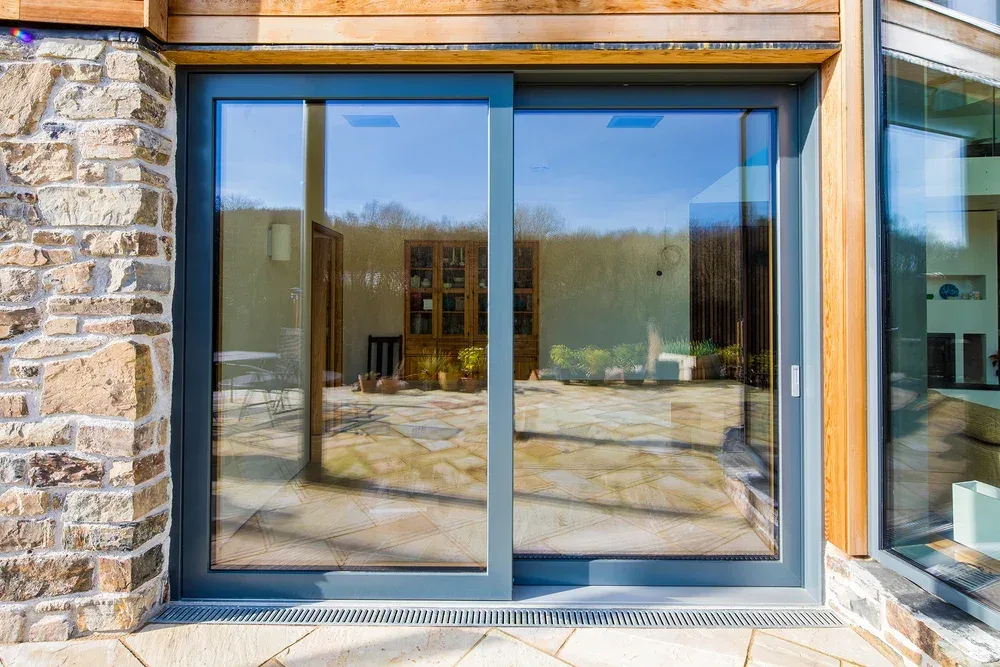 Dark grey aluminium sliding patio doors in a stone and timber-clad home