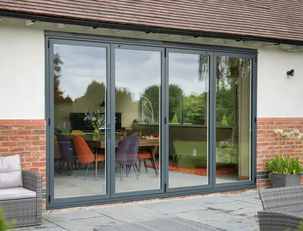Slate grey RAL 7015 aluminium bi-fold doors on a brick and render house, looking into a dining room
