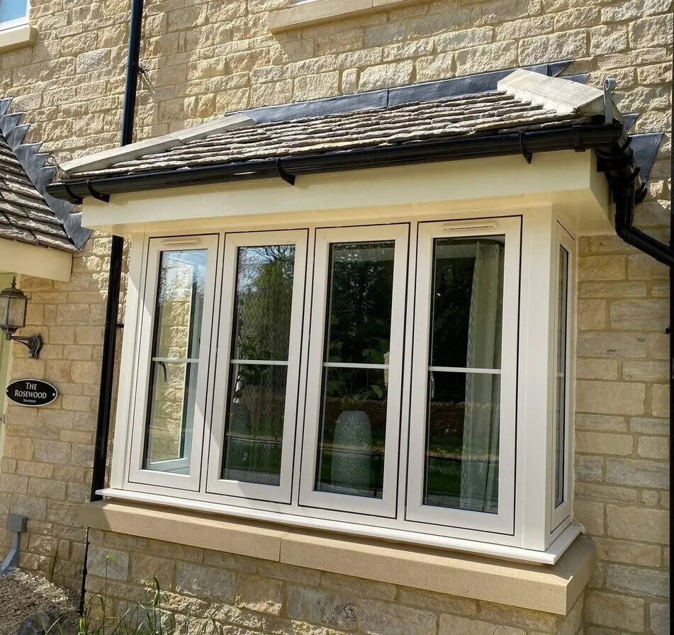 Cream uPVC square bay window with a tiled canopy roof on a stone-built house