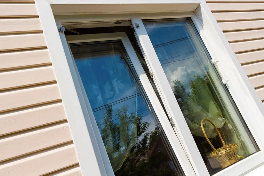 White uPVC tilt and turn window standing open in a wall of beige weatherboard cladding